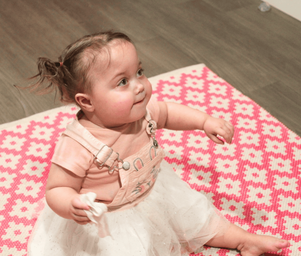 Child sitting down on a rug looking up while smiling