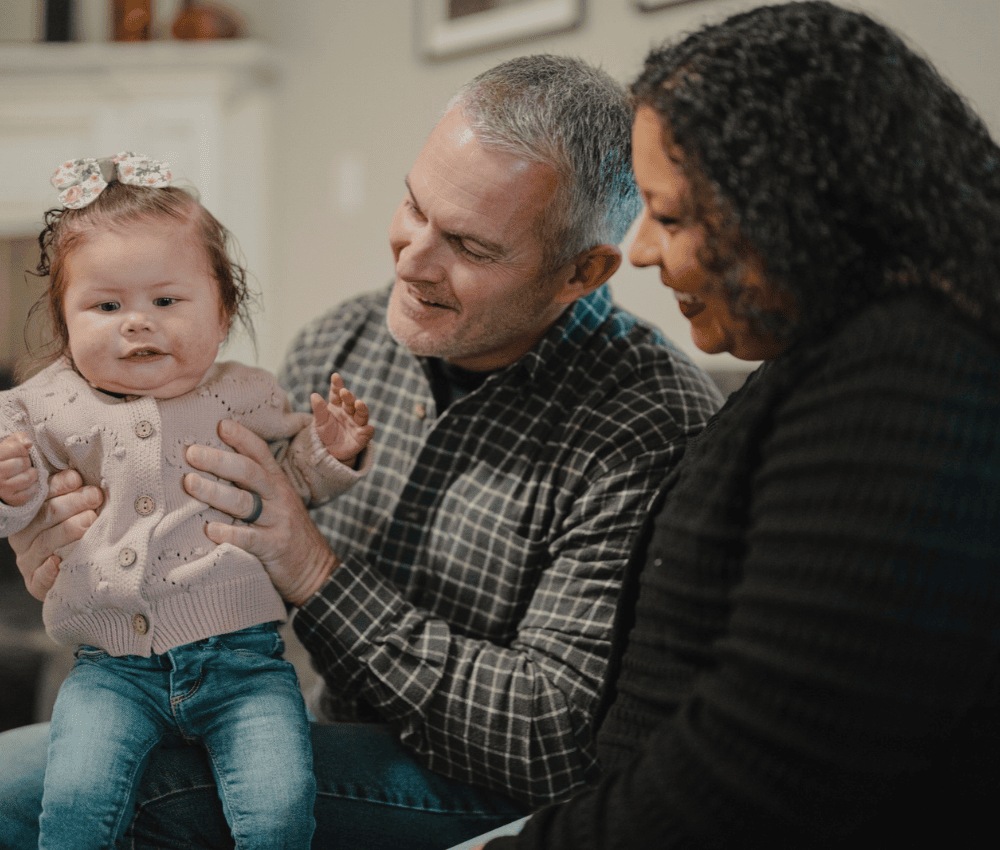 Mom and dad holding a toddler and looking at her.